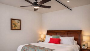 Een netjes opgemaakt slaapkamer met een houten hoofdbord, een bed met witte lakens, een rode plaid en twee bedlampjes.