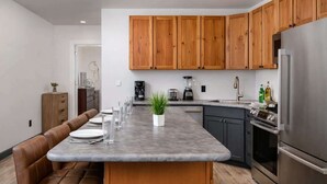 Een moderne keuken met houten kasten, een centraal eiland met zitplaatsen, een inbouwoven en een roestvrijstalen koelkast.