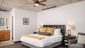Ein modernes Schlafzimmer mit einem großen Bett, Nachttischlampen, einem Deckenventilator und Blick ins Badezimmer.