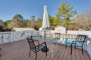 A wooden deck with a glass table and chairs, a pool, and a white fence.
