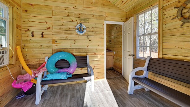 L’intérieur d’une cabane avec des murs en bois, un banc, une fenêtre et une porte.
