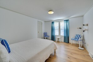 A bedroom with a bed, two chairs, a small table, and a window with curtains.