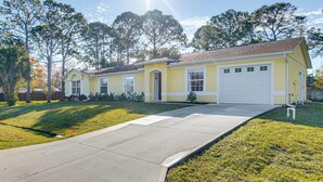 Une maison jaune de plain-pied, avec un garage à l’avant, une allée et une pelouse.