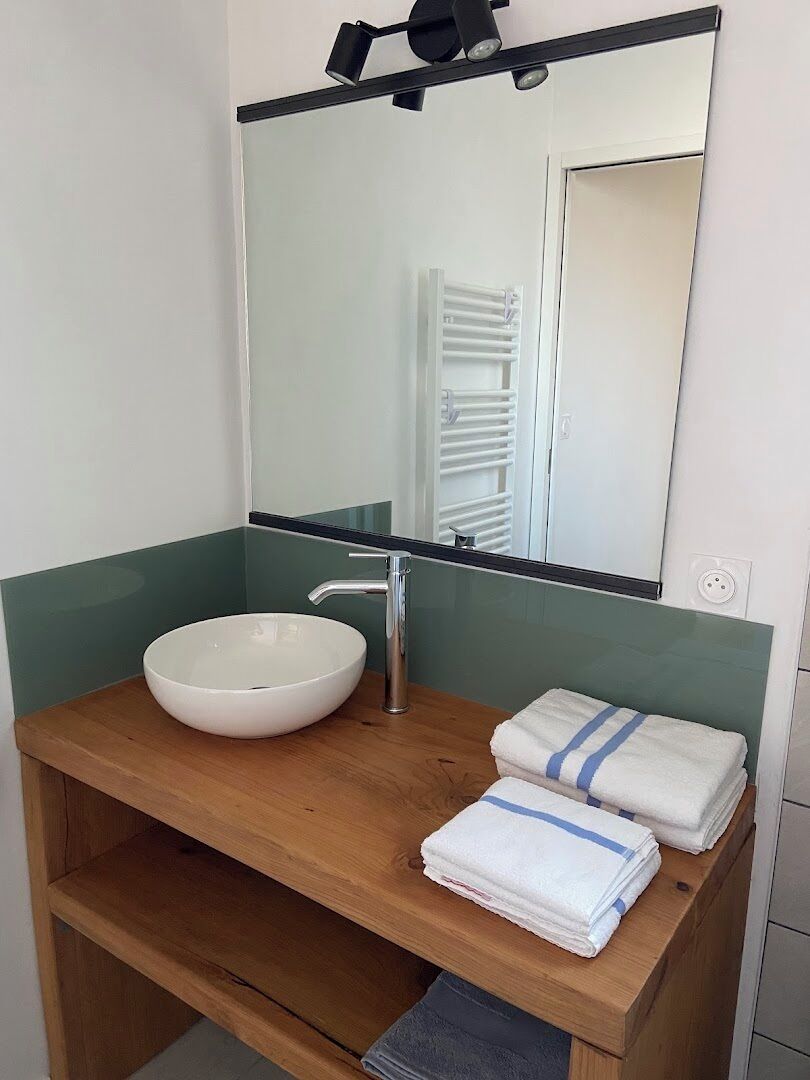 Une salle de bain avec un lavabo rond blanc, un miroir et un porte-serviettes avec des serviettes pliées.
