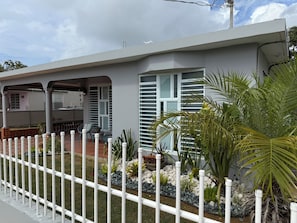 A modern house with a covered patio, a white fence, and a garden with various plants. - Hernández Rental -complete house- (Aguadilla)