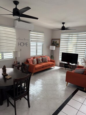 A living room with a sofa, TV, ceiling fans, and a dining table. - Hernández Rental -complete house- (Aguadilla)