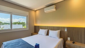 A hotel room with a bed, a nightstand, an air conditioning unit, and a window with a view of greenery. - Apt 260m From Mundo do Vapor Dal0417 (Canela)