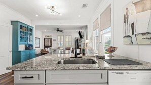 A kitchen with a granite countertop, white cabinets, and a dishwasher. There is a dining area with a table and chairs, and a ceiling fan.