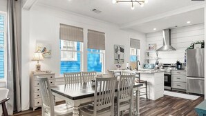 A modern kitchen with white cabinetry, a stainless steel refrigerator, and a dining area with a wooden table and chairs.