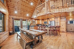 A wooden cabin with a dining area, kitchen, and a balcony. - Fantastic 5-bedroom/Hot Tub/Pool Table/Games/Fire Pit/Foosball/Shuffleboard (Broken Bow)