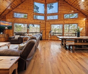 A cabin interior with a wooden ceiling, multiple windows, a sofa, a dining table, and a telescope. - Fantastic 5-bedroom/Hot Tub/Pool Table/Games/Fire Pit/Foosball/Shuffleboard (Broken Bow)
