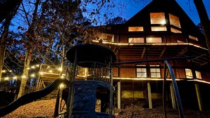 A wooden cabin with multiple windows, a play structure, and string lights. - Fantastic 5-bedroom/Hot Tub/Pool Table/Games/Fire Pit/Foosball/Shuffleboard (Broken Bow)