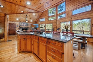 A spacious cabin interior with a large wooden dining table, a kitchen area, and a fireplace. - Fantastic 5-bedroom/Hot Tub/Pool Table/Games/Fire Pit/Foosball/Shuffleboard (Broken Bow)