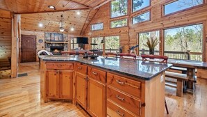 A spacious kitchen with wooden cabinets, a large island, and multiple windows offering views of the outdoors. - Fantastic 5-bedroom/Hot Tub/Pool Table/Games/Fire Pit/Foosball/Shuffleboard (Broken Bow)