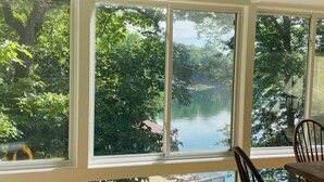 Ein Zimmer mit großen Fenstern mit Blick auf einen See, ein Holztisch und Stühle. Ein Schild über dem Tisch zeigt: 'WELCOME TO THE LAKE'.
