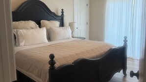 Ein Schlafzimmer mit einem Bett, einem Deckenventilator, einer Tür und einem Fenster mit Vorhängen.
