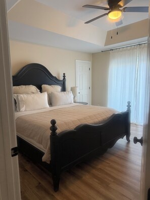 Ein Schlafzimmer mit einem Bett, einem Deckenventilator, einer Tür und einem Fenster mit Vorhängen.