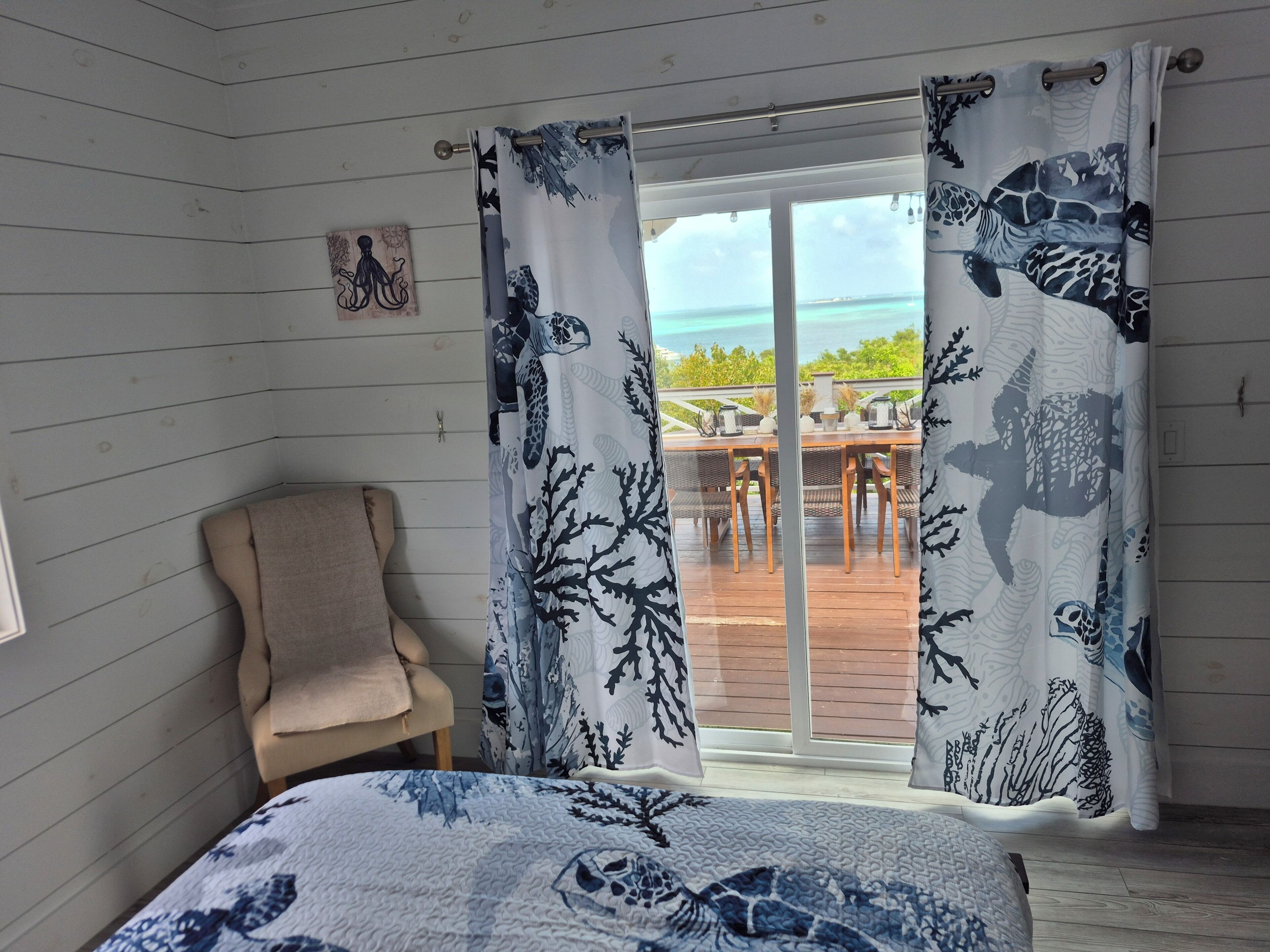 Una habitación con cama, una silla y vista al océano tras cortinas.