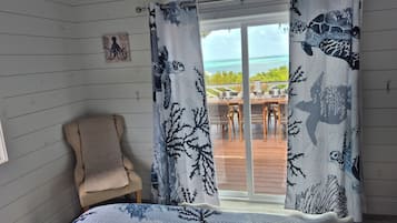 Una habitación con cama, una silla y vista al océano tras cortinas.