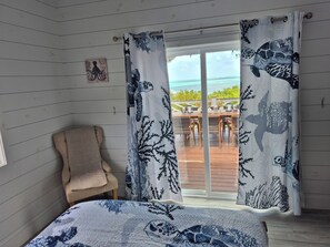 Een kamer met een bed, een stoel en uitzicht op de oceaan door gordijnen.