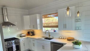Eine moderne Küche mit weißen Schränken, Edelstahlgeräten, einem Backofen, einer Spüle und einem Fenster mit Jalousien.