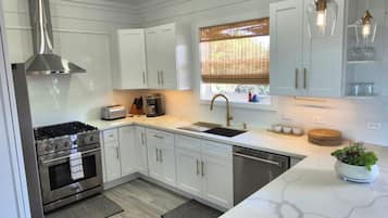 Una cocina moderna con armarios blancos, electrodomésticos de acero inoxidable y una ventana con persianas.