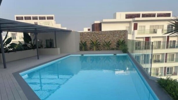 Una piscina en la azotea con terraza de madera, rodeada por edificios modernos.