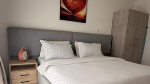 Un dormitorio moderno con una cama grande, una mesita de noche con un reloj, un armario y un cuadro colgado en la pared.