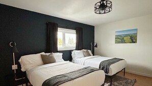 Ein Schlafzimmer mit zwei Betten, einem großen Fenster, Blick auf die Landschaft und einem modernen Kronleuchter.