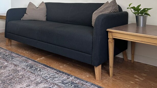 Una sala de estar moderna con un sofá azul oscuro, dos almohadones estampados, una pequeña mesita de madera con una planta en maceta, y un cuadro grande con una noche estrellada en la pared.