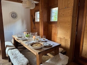 Ein Holztisch gedeckt mit Tellern, Gläsern und Kerzen, mit Bänken und einer Uhr an der Wand.