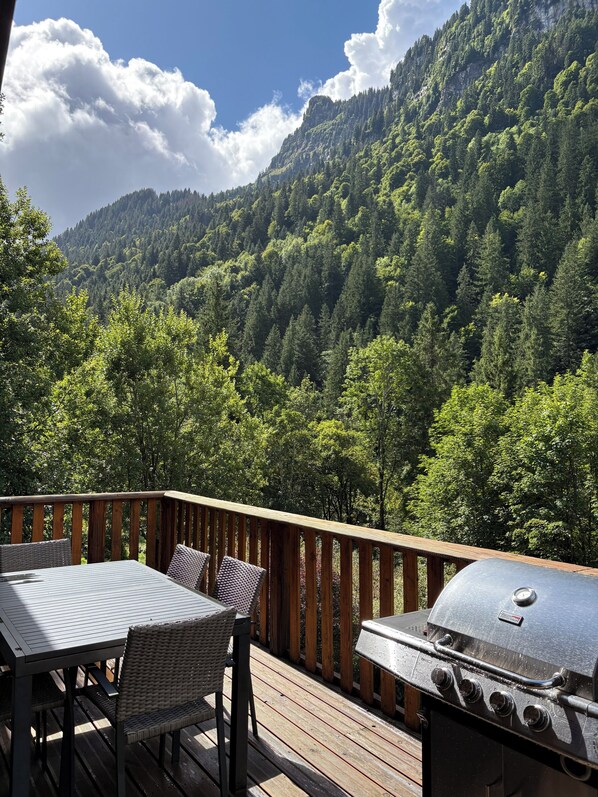 Eine Terrasse mit Tisch, Stühlen, einem Grill und Blick auf einen bewaldeten Berg.