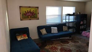 A living room with a blue sofa, a small armchair, a bookshelf, and a framed picture on the wall. - Cute 3 BR- Great for families/kids/pets! (Killeen)