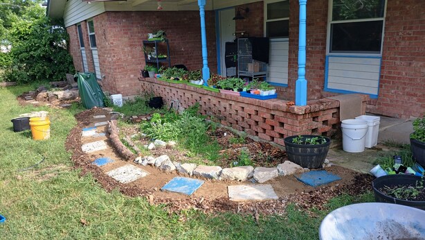 A brick house with a porch, a garden bed with plants, and a wheelbarrow filled with soil. - Cute 3 BR- Great for families/kids/pets! (Killeen)