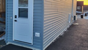 Una construcción de un piso con una puerta blanca y dos ventanas iluminadas, con techo inclinado y entrada de grava.