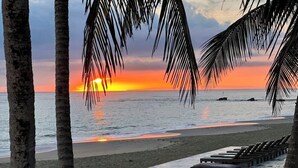 A beach with a sunset, palm trees, and a wooden deck with lounge chairs and pillows. - Charming loft by the sea KiteBeach Condo ByLucia (kite beach)