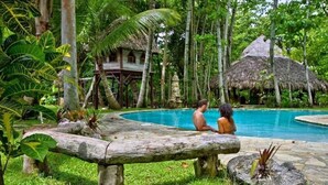 A pool area with a thatched-roof structure, surrounded by lush greenery and a wooden bench. - Charming loft by the sea KiteBeach Condo ByLucia (kite beach)