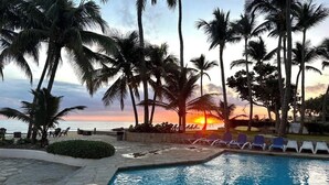 A pool area with palm trees and a sunset view. - Charming loft by the sea KiteBeach Condo ByLucia (kite beach)