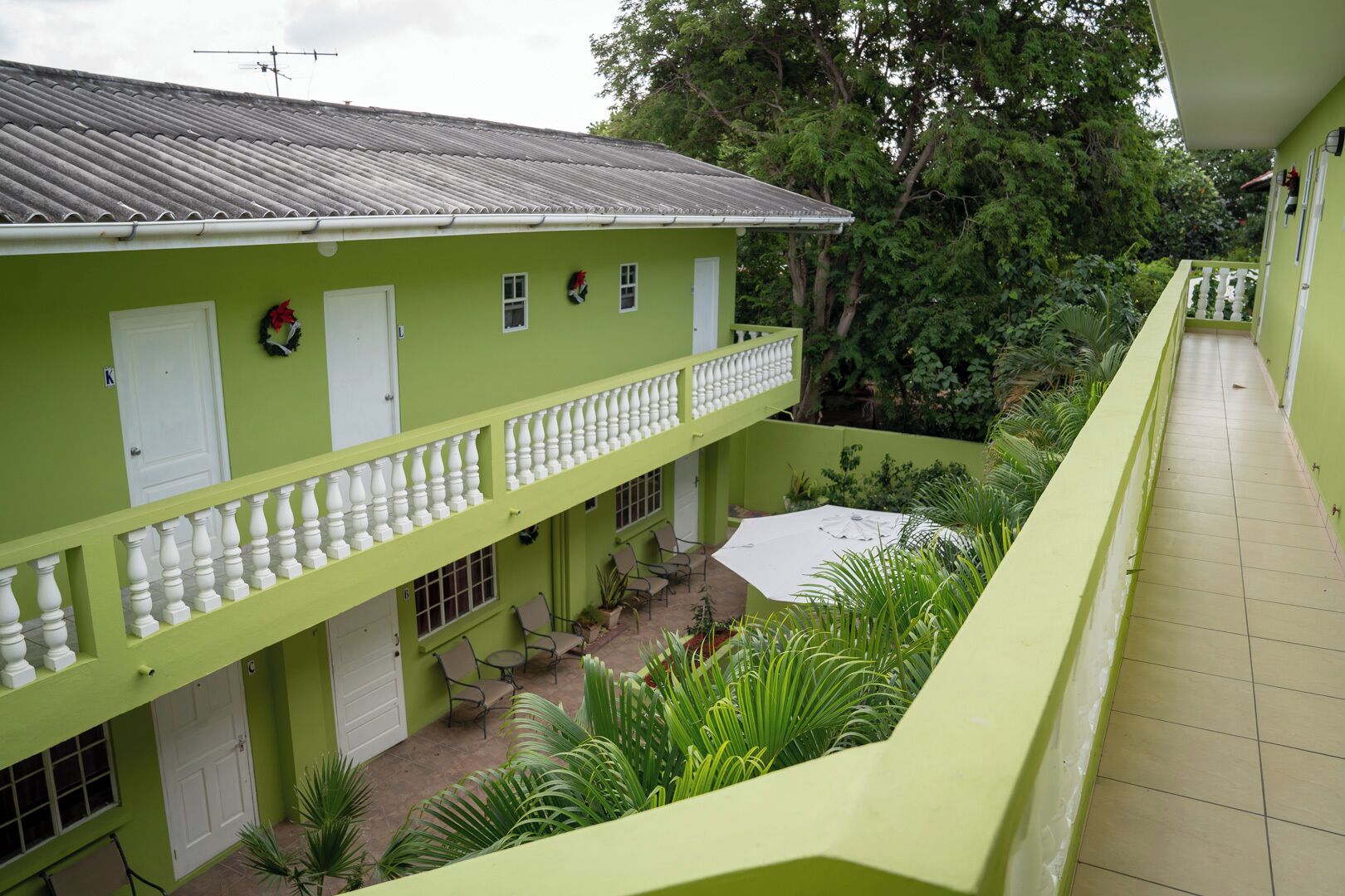 A green building with a balcony, a covered patio area, and surrounding greenery.