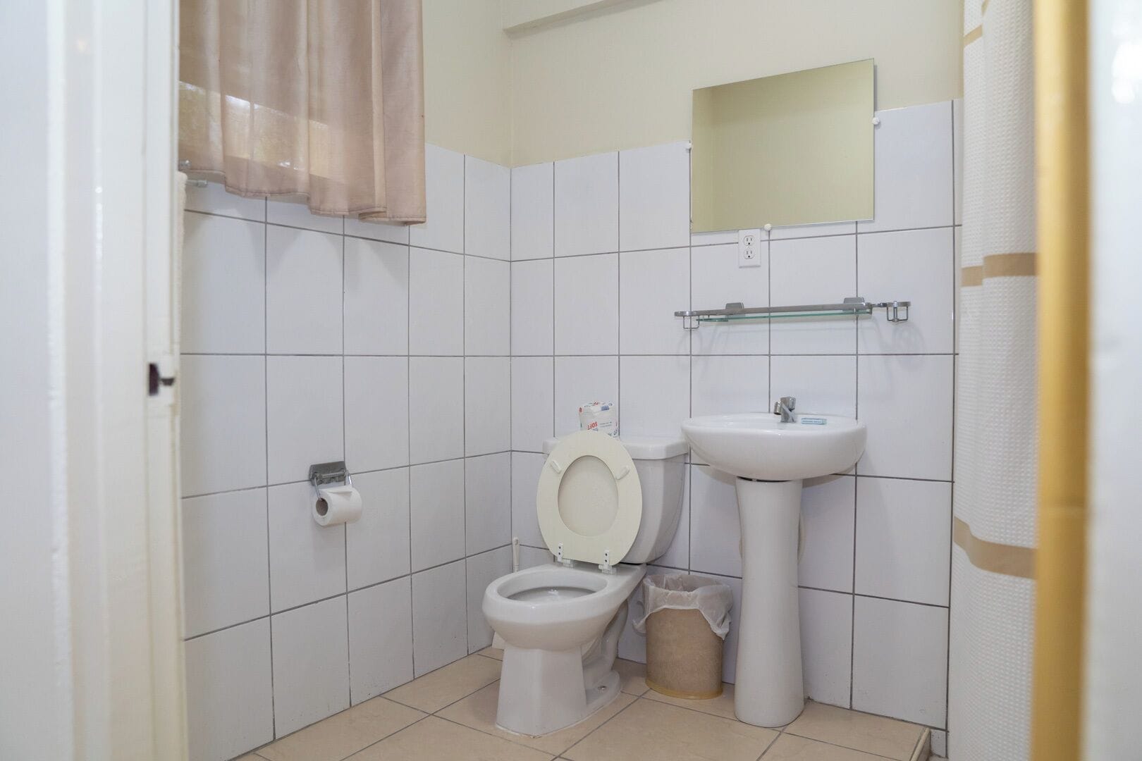 A small, clean bathroom with white tiles, a toilet, a sink, and a mirror.