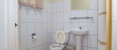 A small, clean bathroom with white tiles, a toilet, a sink, and a mirror.