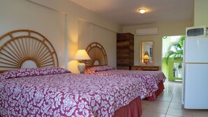A hotel room with two beds, a wooden headboard, a bedside lamp, a mirror, a wardrobe, and a refrigerator. - Apartamentu Holanda (Willemstad)