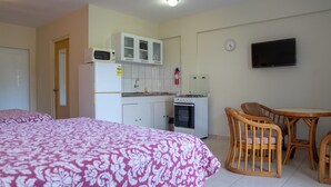 A hotel room with two beds, a kitchenette, a dining area with wicker chairs, and a flat-screen TV on the wall. - Apartamentu Holanda (Willemstad)