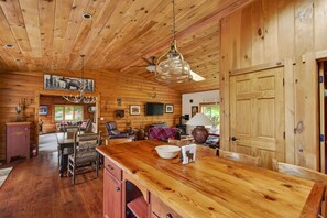 A wooden cabin interior with a dining area, kitchen, and a large wooden door. - Pet friendly log cabin in the heart of the Catskills that can sleep 13 people! (Roxbury)