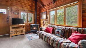 Ein Blockhaus-Interieur mit einer Couch, einem Fernseher und einem Holzofen.