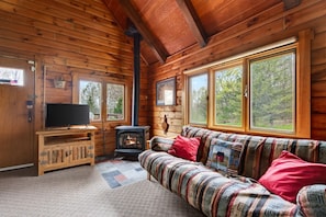 A log cabin interior with a sofa, TV, and wood-burning stove. - Pet friendly log cabin in the heart of the Catskills that can sleep 13 people! (Roxbury)