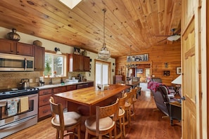 A log cabin interior with a wooden dining table, chairs, a kitchen with a microwave, and a fireplace. - Pet friendly log cabin in the heart of the Catskills that can sleep 13 people! (Roxbury)