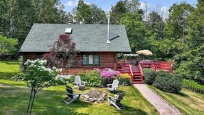Eine Hütte mit geneigtem Dach, einem Schornstein und einer Terrasse mit Sitzgelegenheit.