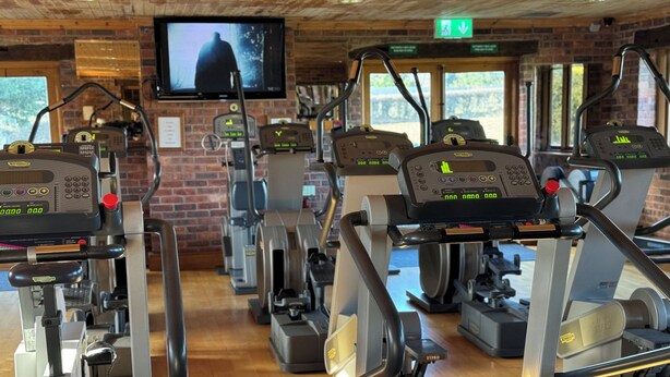 Ett gym med flera konditionsträningsmaskiner, en tv-skärm och en vägg av tegelsten.