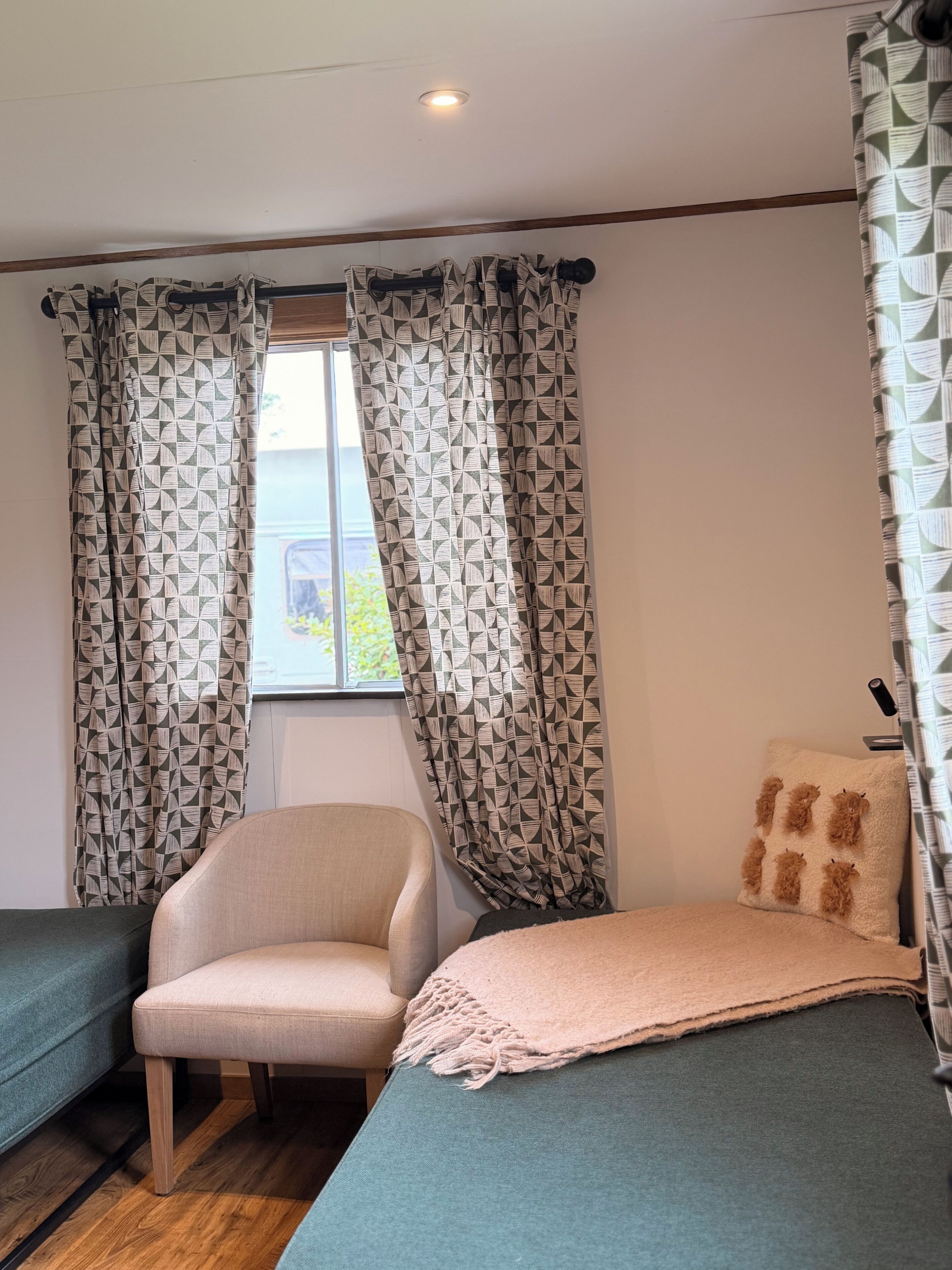 A room with a bed, a chair, and a window with patterned curtains.